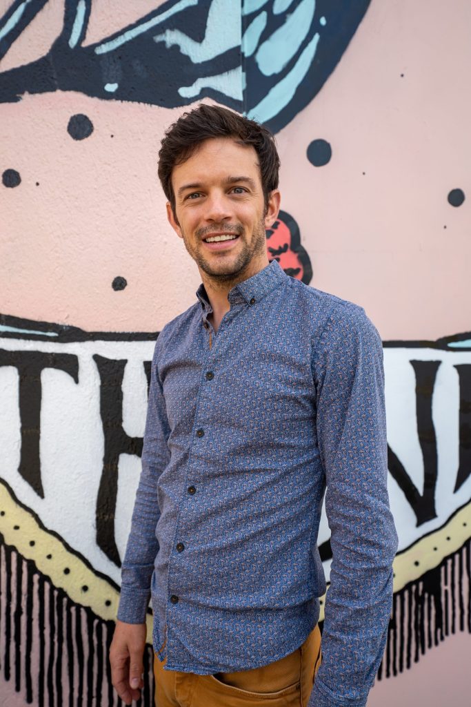 Portrait en plan américain de Gaëtan Le Poupon devant un mur d'artiste